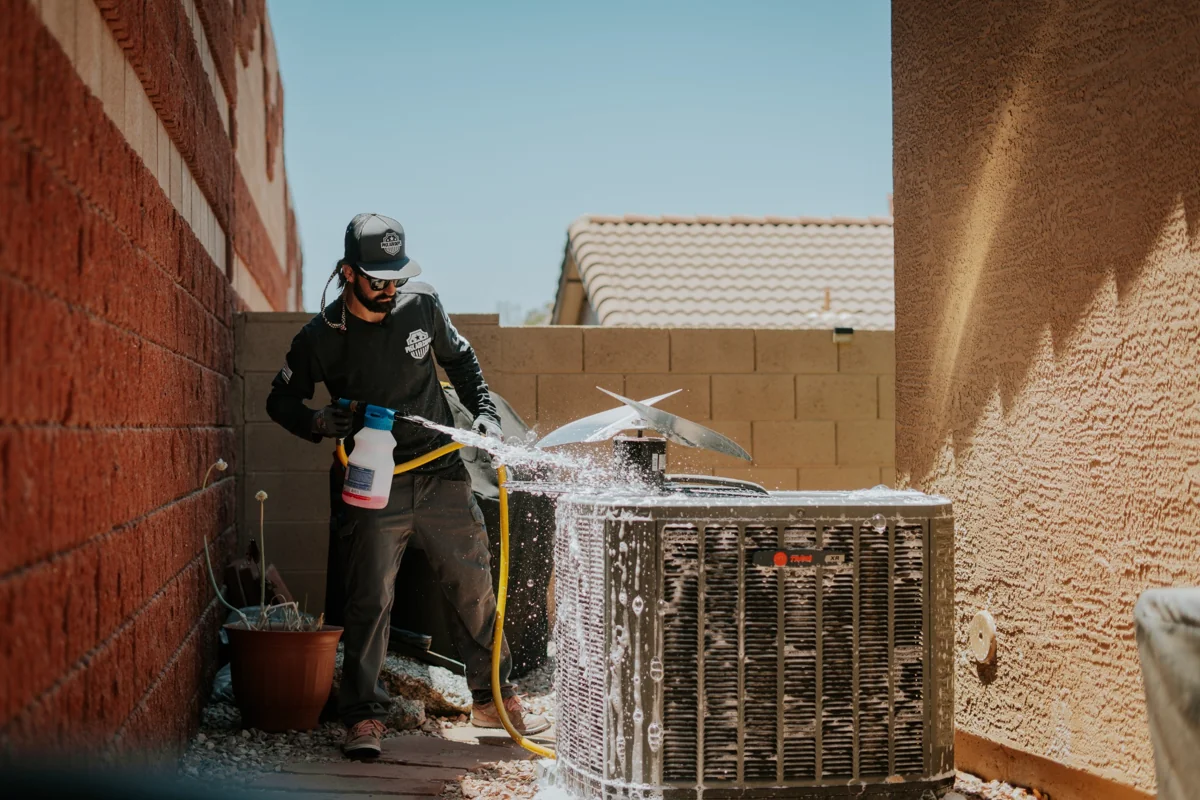 Technician rinsing the exposed condenser coil with a hose