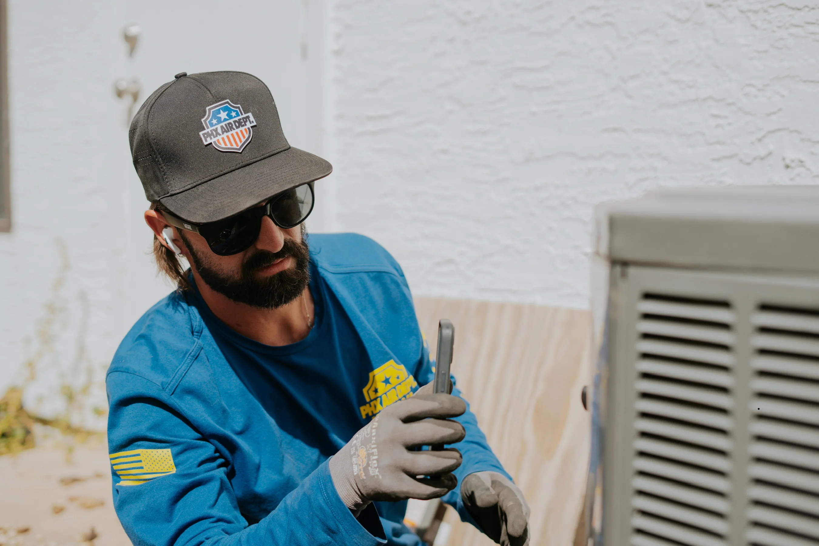 Phoenix Air Department technician checking diagnostics on a phone at an outdoor AC unit